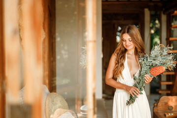 Bride waiting for the big moment. Young bride in beautiful dress holding bouquet of flowers posing near window at home. Wedding concept