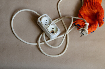 Hand wearing a protective orange glove holds an electrical plug after  fire