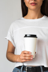 young woman wearing white t-shirt and blue jeans and holding white disposable paper coffee cup on white background