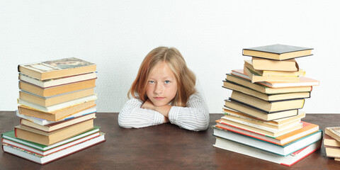 Portrait of a teenage girl who sits at a table among the books. Looks into the camera. Isolated background.