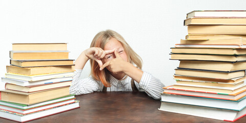 Portrait of a teenage girl sitting at a table tired among the books. Looks through a hand-made frame. Isolated background.
