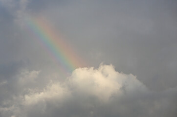 Fototapeta na wymiar A short rainbow high in the dark clouds