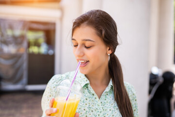 Young woman smiling and drinking cocktail with ice in plastic cup with straw