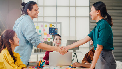 Obraz premium Multiracial group of young creative people in smart casual wear discussing business shaking hands together and smiling while standing in modern office. Partner cooperation, coworker teamwork concept.