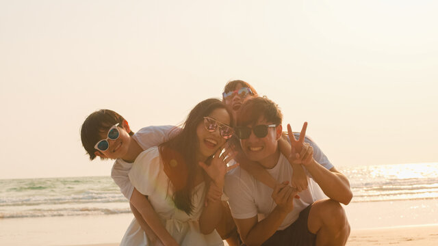 Asian young happy family enjoy vacation on beach in the evening. Dad, mom and kid set camera for take photo while relax together near sea when sunset. Lifestyle travel holiday vacation summer concept.