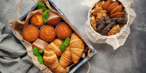 Maffins and croissants in a wooden tray on a grey background. Top view