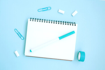 Back to school flat lay with white open notebook, marker, clips and scotch on a blue background with space for text. Getting ready for school. Creative workspace with stationery