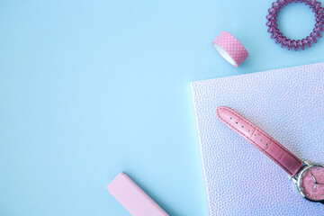 Pink set for girls. Neon notebook, scotch tape, watch, eraser and hair tie on a blue background with space for text. School stationery. Getting ready for school. Creative workspace. Flat lay