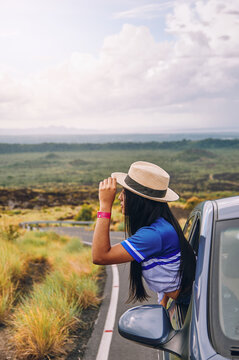Young female wearing a hat leaning out of a car window with a beautiful landscape in the background