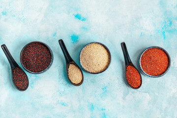 Bowls and spoons with different quinoa on color background