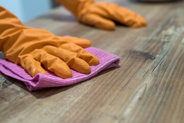 woman wearing rubber gloves and cleaning the kitchen cabinets or surface