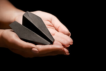 Female hands with paper airplane on dark background. Racism concept
