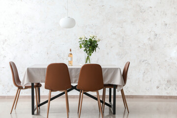 Dining table with wine and bouquet of flowers near light wall