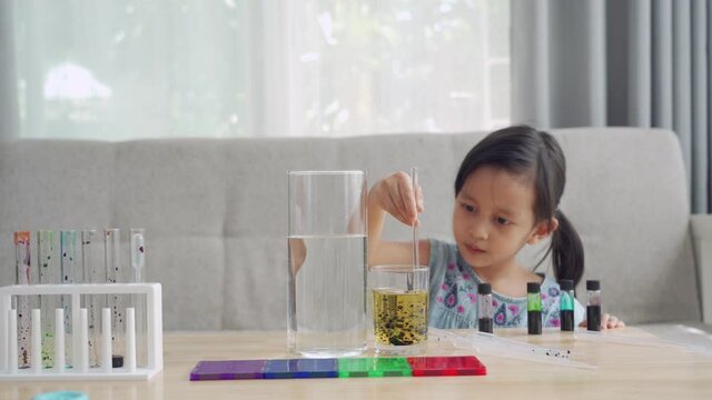A 5 years old of asian little girl is mixing the food color droplets in the oil liquid to prepare experiment of diffusion in the water-oil liquid layer, concept of scientific learning activity at home