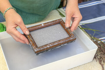 Woman holding frame for making paper sheets from waste paper pulp. Selective focus. Decorative and applied art. Recycling concept, ecology.