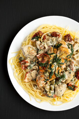 Homemade Creamy Tuscan Chicken with Pasta on a white plate on a black surface, top view. Flat lay, overhead, from above.