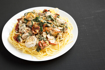 Homemade Creamy Tuscan Chicken with Pasta on a white plate on a black surface, side view. Copy space.