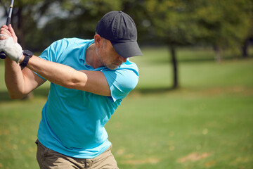 Male golfer swinging at the ball with a driver as he takes his shot on a golf course in a closeup...