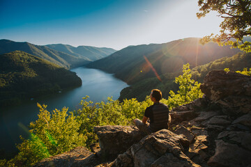 Traveler enjoying sunset on a cliff with a beautiful view of a lake. 