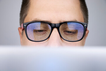 The programmer's glasses reflect lines of code. Programming, development of applications, sites and...
