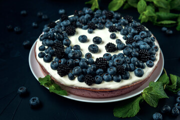 Cottage cheese casserole decorated with blackberry, blueberry and mint leaves on dark textured background.