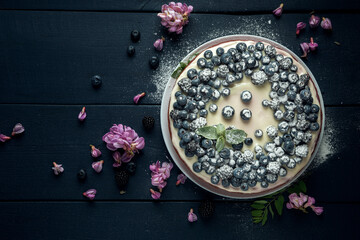 Obraz na płótnie Canvas Cottage cheese casserole with blackberry and blueberry sprinkled with icing sugar and decorated with acacia flowers. Flat lay. Copy space.