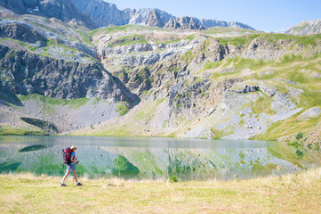 Fototapeta na wymiar Young mountaineer walking next to the sabocos lake in the Pyrenees of Huesca. Reflection of mountains in the lake
