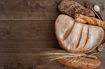 The bakery, several different fresh loaves of bread with a crisp crust, sprinkled with seeds and sesame seeds on a wooden background with boils of wheat.