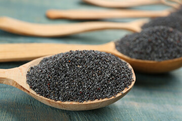 Poppy seeds in spoons on blue wooden table, closeup