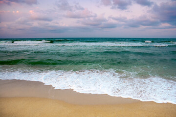 dramatic weather on the seashore. green waves crashing on the beach. cloudy purple sky in evening light