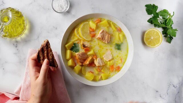 Top view of unrecognisable woman eating delcious salmon soup with carrots, potato and parsley on white background. 4K UHD video.
