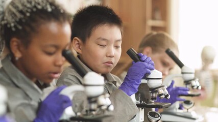 lesson in a modern school, kids look at microscopes in a chemistry lesson, the process of teaching children in a modern school. - Powered by Adobe