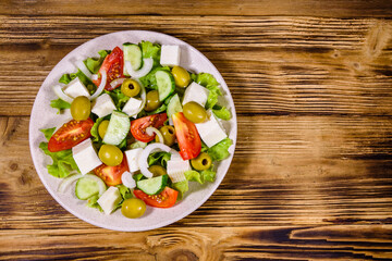 Ceramic plate with greek salad on wooden table. Top view