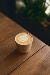 Cup of cappuccino with latte art on the wooden table. Beautiful foam and ceramic cup