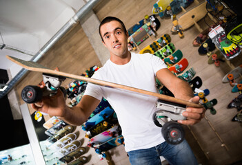 Portrait of glad positive man choosing skateboard in sporting goods store. - Powered by Adobe