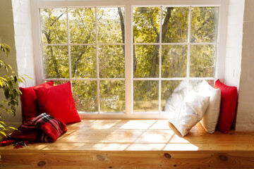 Forest with autumn colors seen through a window , windowsill with red and white pillows