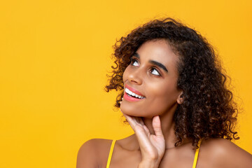 Close up portrait of smiling beautiful Afican American woman thinking looking up isolated on yellow background