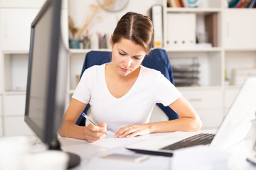 Portrait of busy female entrepreneur sitting at office desk with papers and laptop ..