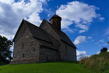 Fototapeta premium Gran, Norway - Aug. 27th 2020: The medieval church Tingelstad Kirke sitting alone on a hilltop overseeing the area of Hadeland in Norway.