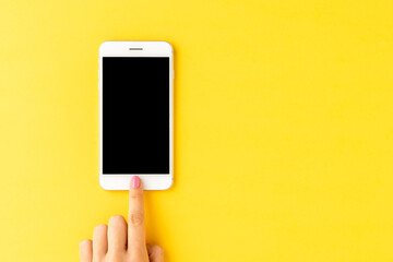 Female hand using smartphone with empty screen on yellow background. Top view