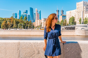 A young woman stands on the embankment with a view of the skyscrapers of Moscow