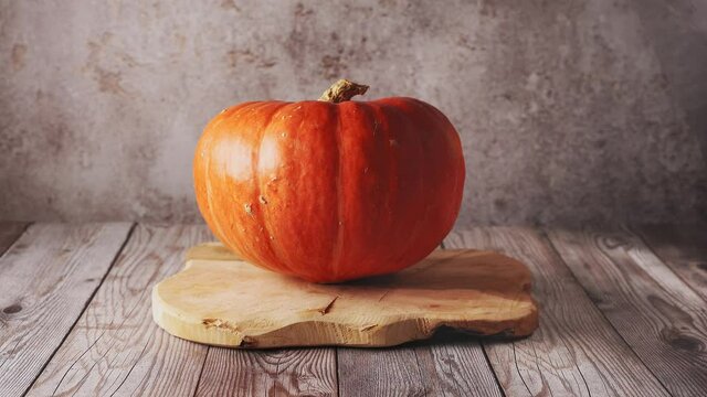 Female hand placing a big orange pumpkin on wooden board in rustic background. Autumn concept. Thanksgiving day. Harvest. 4K UHD