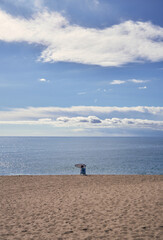 person in the distance sitting alone on the shore of the beach with no one else around