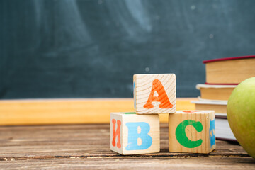 Books and cubes with the letters ABC on wooden table against the background of the chalkboard. Back to school
