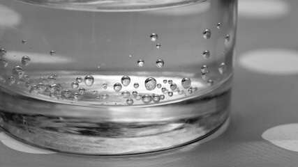 Glass of water with water bubbles. Closeup. Natural mineral water beverage product. Healthy drink. A glass with sparkling water. Panoramic view, black and white 