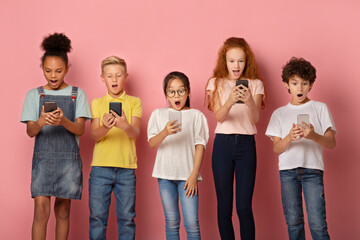 Shocked schoolkids looking into their mobile phones on pink background - Powered by Adobe