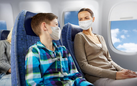 Tourism, Travel And Pandemic Concept - Happy Mother And Son Wearing Face Protective Medical Masks For Protection From Virus Disease Sitting In Plane And Talking Over Porthole Background