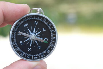 classic navigation compass in hand in summer against background of sandy beach as symbol of tourism...