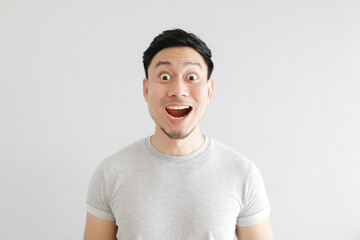 Shocked face of Asian man in grey t-shirt and grey background.