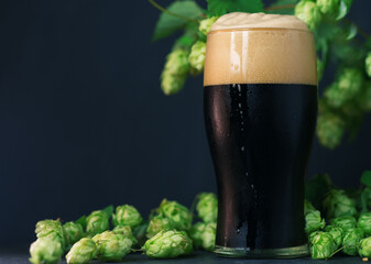 A glass of dark beer, craft stout or porter with green hop cones